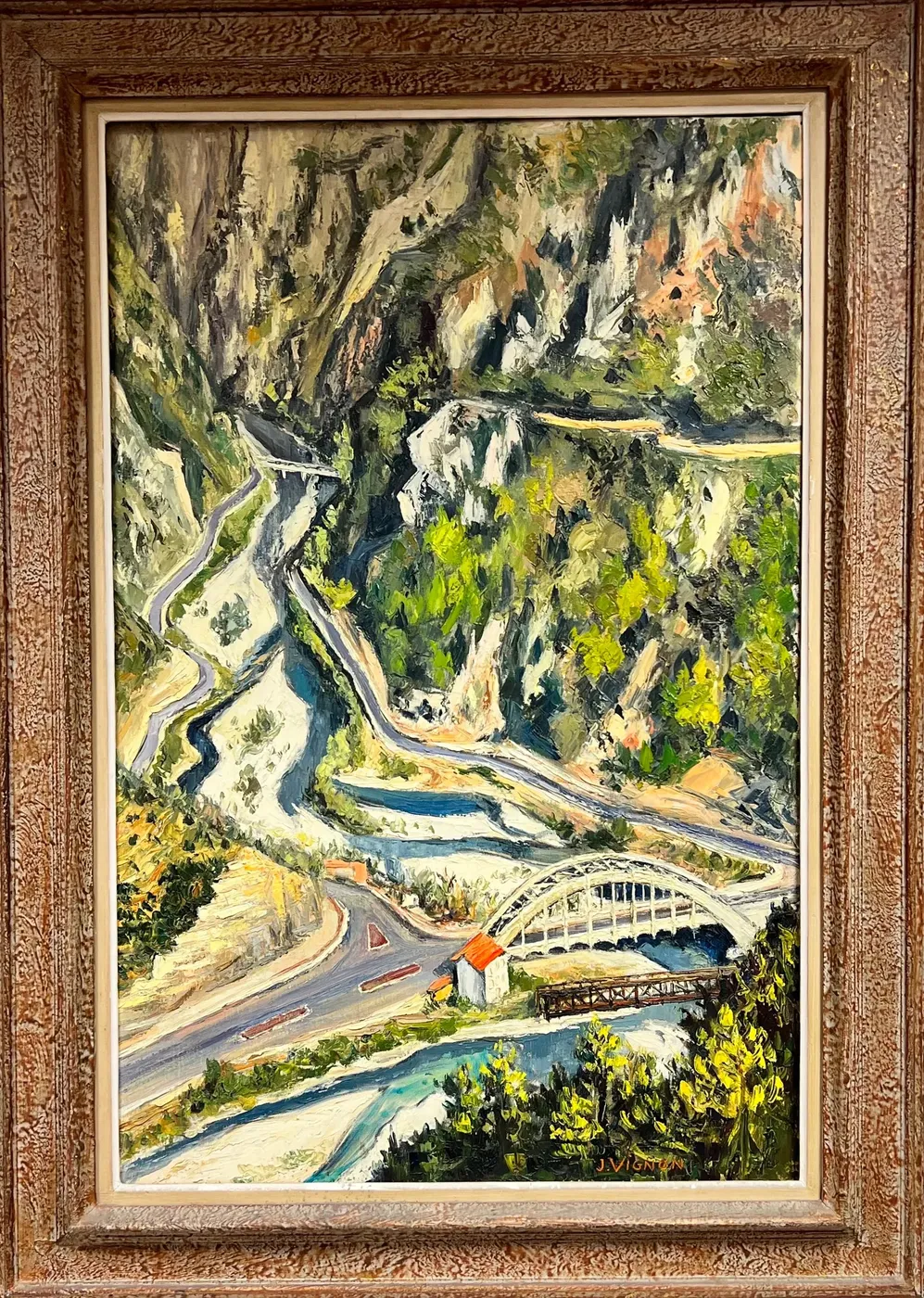 A gorge seen from high above: a pale river braiding through it, a road switchbacking down, and a white steel arch bridge at the bottom.