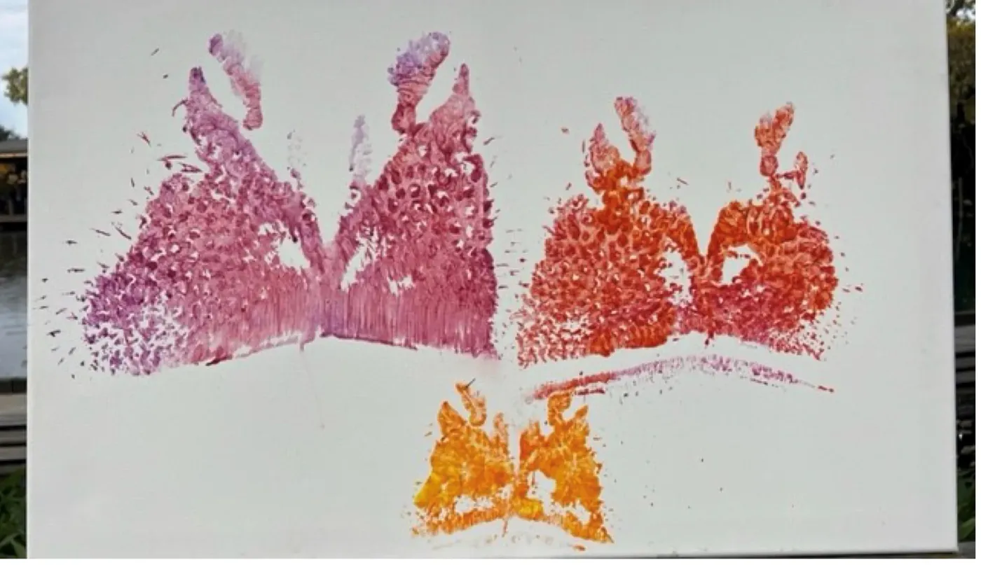 Three symmetrical prints on white canvas, made by pressing painted hippopotamus snouts to the surface: a large magenta pair, a red-orange pair, and a small gold one below.